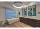 Bathroom with modern chandelier, soaking tub, dual sink vanity, and large window with coverings at 1900 Vero Dr, Las Vegas, NV 89134