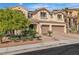 Two-story tan home featuring a tile roof, balcony, paver driveway and a two-car garage with mature landscaping at 9967 Pipestone St, Las Vegas, NV 89141