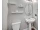 Cozy powder room with pedestal sink, oval mirror, toilet, and decorative shelves for storage and display at 10397 Skye Canyon Falls Ave, Las Vegas, NV 89166
