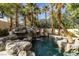 Beautiful rock waterfall flows into the sparkling pool, surrounded by palm trees and mature landscaping at 1301 Kingdom St, Las Vegas, NV 89117