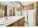 Bright bathroom featuring dual sinks, a large mirror, wood cabinets, and a glass-enclosed shower at 4956 Momenti St, Las Vegas, NV 89135