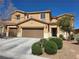 Tan two-story home featuring a two-car garage, manicured front yard with shrubs, and a well-maintained desert landscape at 6656 Fort William St, North Las Vegas, NV 89084