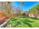 Landscaped backyard with a small lawn, various trees, plants, and a brick wall under a bright blue sky at 4921 Lazy Day Ct, Las Vegas, NV 89131