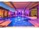Luxury pool area featuring a covered lounge area, lush plants, ambient lighting, and pergola creating a tranquil outdoor retreat at 7311 Velvet Sky St, Las Vegas, NV 89131