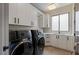 Modern laundry room with black front load washer and dryer, sleek white cabinetry, and a window for natural light at 505 Dragon Gate Ct, Henderson, NV 89012