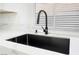 Close-up of black kitchen sink with stainless steel faucet and white countertop next to a window at 80 Sea Holly Way, Henderson, NV 89074