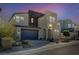 This modern two-story home boasts desert landscaping, a gray garage door, and an arched entryway at dusk at 2132 Ponticino St, Henderson, NV 89044