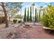 Backyard featuring a fire pit, desert landscaping, mature trees, and stone seating under a blue sky at 4775 N Tee Pee Ln, Las Vegas, NV 89129