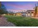Landscaped backyard featuring a lush lawn, mature trees, and a charming Mediterranean-style home at dusk at 4775 N Tee Pee Ln, Las Vegas, NV 89129