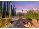 Landscaped backyard features a fire pit, mature trees, desert foliage, and stone benches under a vibrant sky at 4775 N Tee Pee Ln, Las Vegas, NV 89129
