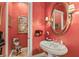 Bright powder room features red accent wall, round mirror, pedestal sink, and decoratively framed art at 4775 N Tee Pee Ln, Las Vegas, NV 89129