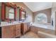 Bathroom featuring dual sinks, jacuzzi tub under decorative glass window, and marble countertops at 10024 Skipper Ct, Las Vegas, NV 89117