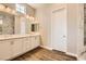 Bright bathroom with double sinks, white cabinetry, wood flooring, and large mirror at 728 Omaggio Pl, Henderson, NV 89011