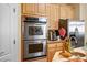 A stainless steel double oven is surrounded by wooden cabinetry, granite countertops and stainless steel refrigerator at 4574 Sheri Lyn Ct, Las Vegas, NV 89121