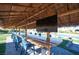 Gorgeous outdoor dining area with a tiki roof, large TV, and seating for many; a stunning pool can be seen in the background at 120 Chartan Ave, Las Vegas, NV 89183