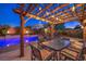 Charming outdoor dining area beneath a string-lit pergola, adjacent to a sparkling pool and lush greenery at 8429 Brackenfield Ave, Las Vegas, NV 89178