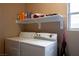A laundry room with a full-size washer and dryer plus an overhead shelf and tan walls at 1163 Regal Lily Way, Las Vegas, NV 89123