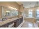 Luxurious bathroom with a large mirror, granite counters, dark wood cabinets, and a soaking tub at 1377 Ruby Sky Ct, Henderson, NV 89052