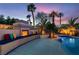 Outdoor fireplace with built-in seating, colorful pillows, tropical landscaping, and access to the pool and spa at 379 Fynn Valley Dr, Las Vegas, NV 89148