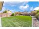 Wide backyard featuring green turf and retaining wall lined with trees and decorative rock at 7322 Dazzle Point St, North Las Vegas, NV 89084