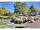 Scenic community pond with rock features, trees, and green space under a bright blue sky at 9005 Feather River Ct, Las Vegas, NV 89117