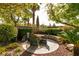 Backyard with tropical landscape, mature trees, and a stone seating area with a table and chairs at 11253 Piper Peak Ln, Las Vegas, NV 89138