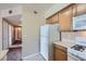 Galley kitchen featuring wooden cabinets, white appliances, and a tiled floor, seamlessly transitioning into a carpeted hallway with multiple doors at 7151 S Durango Dr # 312, Las Vegas, NV 89113
