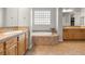 Bright bathroom featuring double sinks, wooden cabinets, and a soaking tub under a glass block window at 6895 Kelp Ledge Ct, Las Vegas, NV 89131