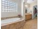 Bright bathroom featuring a soaking tub under a glass block window, wooden cabinets, and a walk-in closet at 6895 Kelp Ledge Ct, Las Vegas, NV 89131