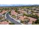 Aerial view showcasing a neighborhood with single-story homes, red tile roofs, lush landscaping, and distant city skyline at 10201 Los Padres Pl, Las Vegas, NV 89134