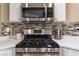 Close-up of gas range stove with stainless steel microwave and mosaic tile backsplash at 4804 Portola Vista Ave, Las Vegas, NV 89139