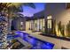 Modern home exterior featuring a unique water feature, lush landscaping, cacti, and a palm tree adorned with lights at 535 Serenity Point Dr, Henderson, NV 89012