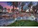 Stunning rock waterfall feature with lush landscaping and palm trees at dusk create backyard paradise at 658 Falcon Summit Ct, Henderson, NV 89012