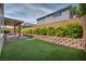 Well-kept backyard featuring green artificial grass, brick retaining wall and a covered patio with a ceiling fan at 9370 Burning Sage Ave, Las Vegas, NV 89149