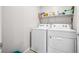 Functional laundry room with modern white washer and dryer appliances, plus a shelf for storage at 9068 Lennon Ln, Las Vegas, NV 89113