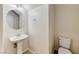 Compact half bath with a pedestal sink, round mirror, and toilet, featuring neutral walls and a light fixture at 7012 Mercurio Ave, Las Vegas, NV 89131