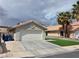 A single-story house featuring a two-car garage, desert landscaping, and mature palm trees at 7091 Rhapsody Ln, Las Vegas, NV 89119