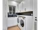 Laundry room with white cabinetry, sleek backsplash, modern washer and dryer, and a large window at 211 Granite Ct, Boulder City, NV 89005