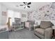 This Bedroom features a large floral accent wall, neutral walls and carpet, and a gray glider and crib at 10365 Cherokee Corner Ave, Las Vegas, NV 89129