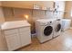 Laundry room with washer, dryer, shelves, white colored walls and accents and tan colored tile flooring at 6493 Yellow Bells Ct, Las Vegas, NV 89131