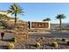 Landscaped Peaks community entrance featuring desert vegetation and palm trees with a stacked stone and metal sign structure at 19 Hilltop Crest St, Henderson, NV 89011