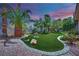 Serene backyard featuring lush green grass, mature landscaping, and decorative rock accents at twilight at 4722 Blue Mesa Way, Las Vegas, NV 89129