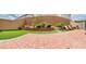 Large backyard featuring a paved patio, artificial turf, a brick wall, and terraced flower beds with plants at 10077 Cooper Mountain St, Las Vegas, NV 89141