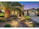 Inviting front entrance with a stone path and a stone facade, enhanced by lush landscaping and evening lighting at 7181 Barton Creek Ct, Las Vegas, NV 89113
