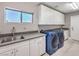 Well-lit laundry room featuring modern blue washer and dryer and a sink with sleek countertops and white cabinets at 5 Clear Crossing Trl, Henderson, NV 89052