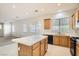 Well-lit kitchen featuring an island, tile countertops, and wooden cabinetry and an adjacent carpeted room at 7568 Shadow Estates Way, Las Vegas, NV 89113