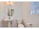 Cozy powder room featuring pedestal sink, round mirror and white toilet with window view at 1129 Paradise Vista Dr, Henderson, NV 89002
