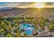 An aerial view displays the community pool, surrounded by lush palm trees, homes and the backdrop of mountains at sunset at 129 Chateau Whistler Ct, Las Vegas, NV 89148