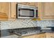 Close-up of kitchen appliances and cabinetry with stone backsplash and dark granite countertops at 437 Via Stretto Ave, Henderson, NV 89011