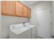 A bright laundry room with white washer and dryer and upper cabinets at 7760 Pine Warbler Way, North Las Vegas, NV 89084